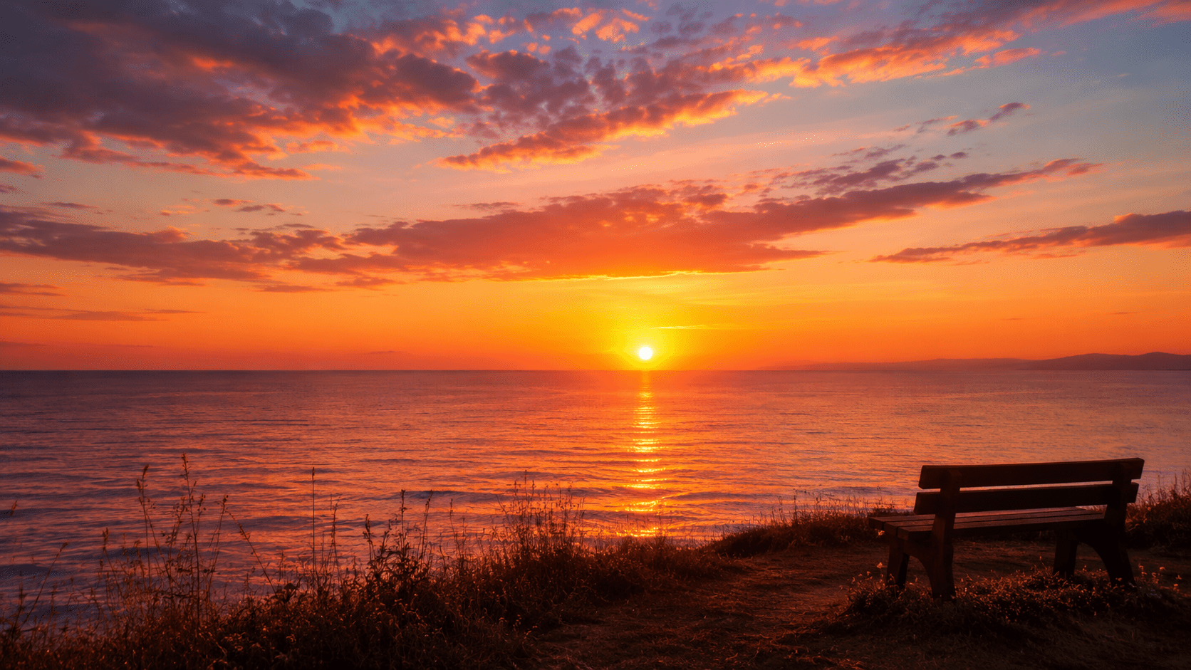 Wooden bench overlooking a calm ocean horizon at sunset beneath a warm golden sky.