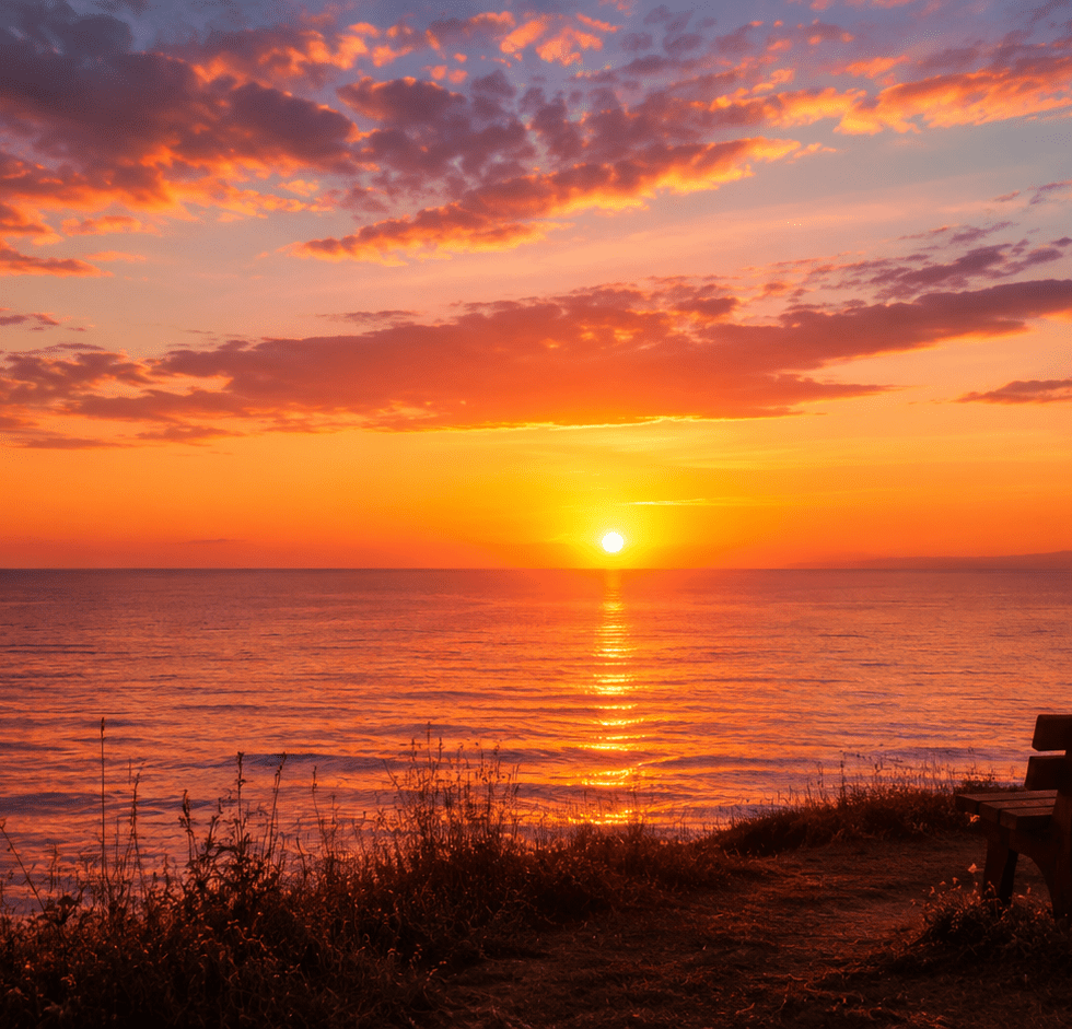 Wooden bench overlooking a calm ocean horizon at sunset beneath a warm golden sky.